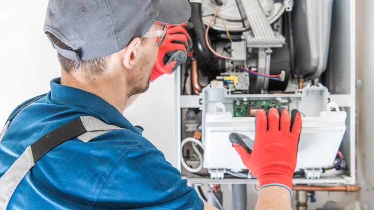 An HVAC technician removes a panel while servicing components inside a furnace unit.