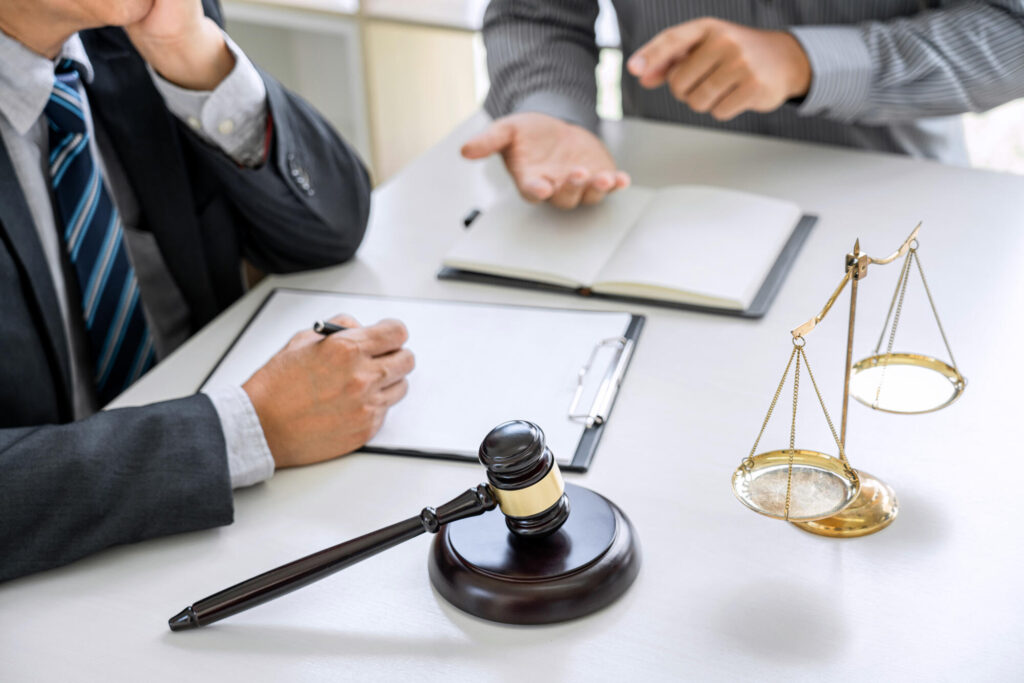 Lawyer consulting with a client at a desk with legal scales and a gavel.
